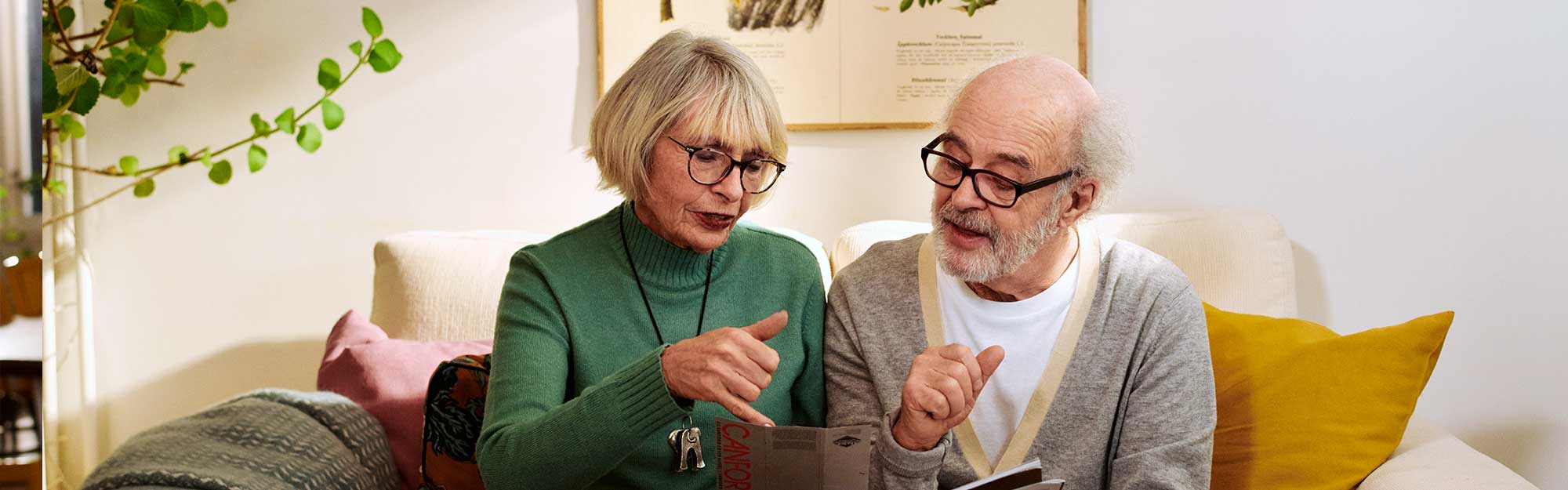 En äldre man och kvinna sitter i en soffa och tittar på en broschyr 